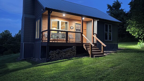 A two-story house with a covered porch, a chimney, and a stack of firewood outside.