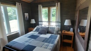 A bedroom with a bed, two bedside tables, two lamps, a ceiling fan, and windows with curtains.