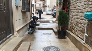 A narrow alleyway with a scooter parked on the left, a potted plant on the right, and a red awning above a door. - Boutique Hotel Grandview (Baku)