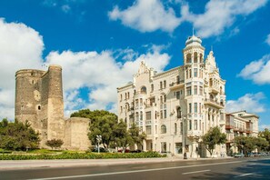 Un edificio histórico con una torre imponente y arquitectura ornamentada, situado junto a una carretera moderna.