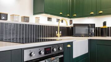 Een moderne keuken met een roestvrijstalen fornuis, een digitaal bedieningspaneel voor de oven, een magnetron en groene keukenkastjes.