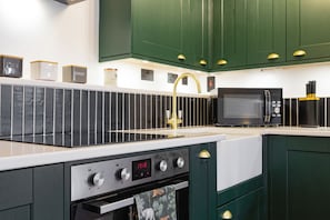 A modern kitchen with a stainless steel range, a digital oven control panel, a microwave, and green cabinetry.