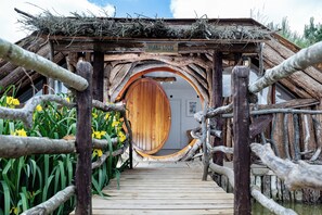 A Hobbit-style house with a wooden door and a wooden bridge leading to it.