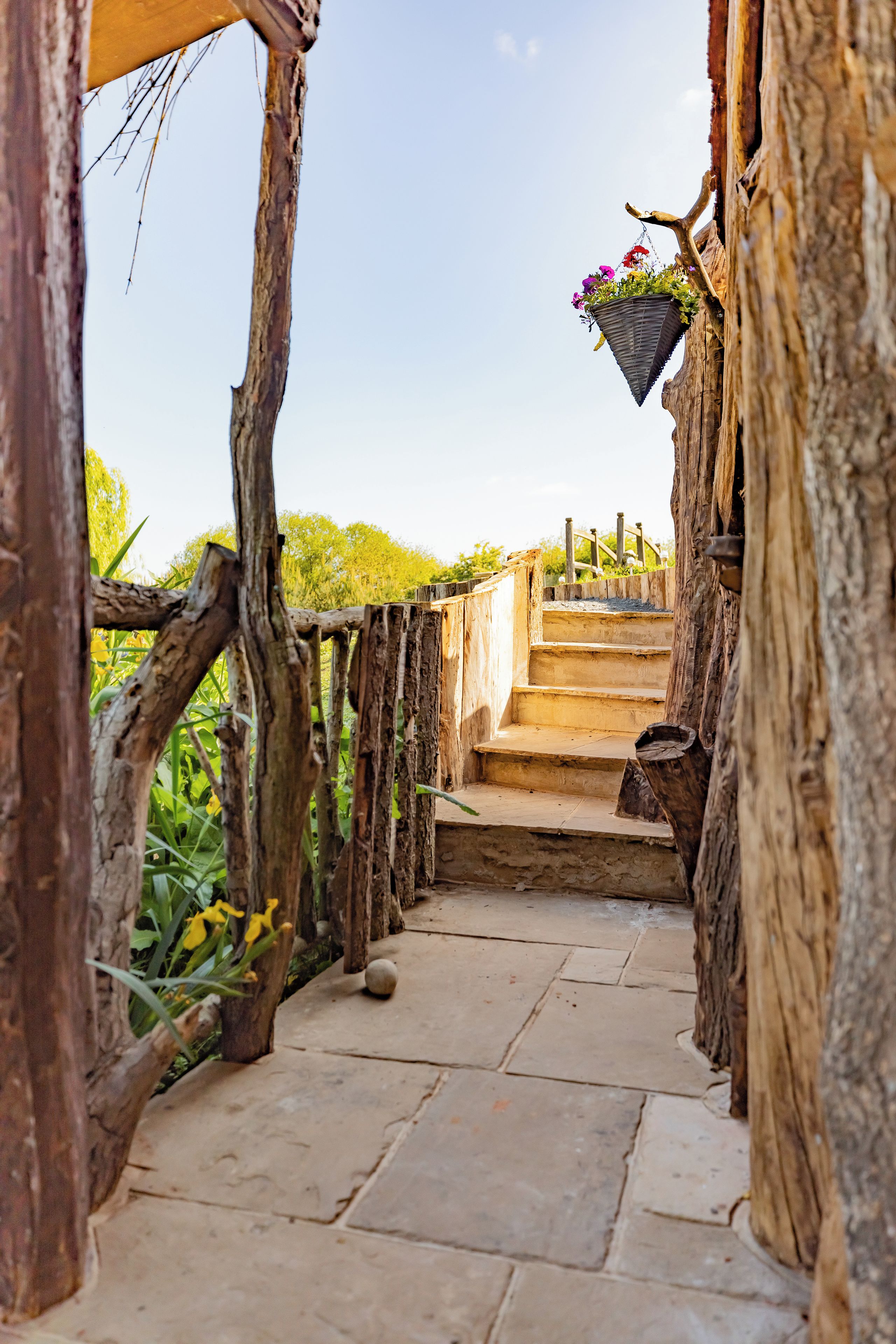 Un escalier en pierre menant à une structure en bois ornée d’un panier à fleurs suspendu.