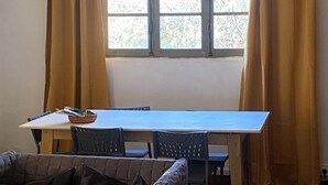 A room with a dining table, chairs, a sofa, and a window with curtains. - Charming wooden house (Auffargis)