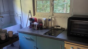 A compact kitchen with a sink, a small refrigerator, a window with a view of greenery, and a chair. - Charming wooden house (Auffargis)