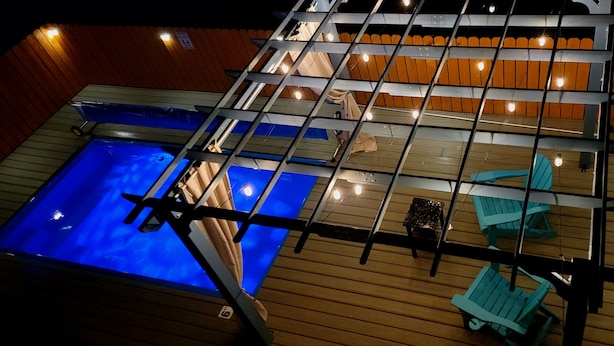 Un espace piscine sur le toit, doté d’une structure en verre, d’une terrasse en bois et de chaises longues.