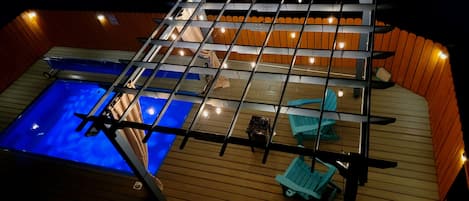 Un espace piscine sur le toit, doté d’une structure en verre, d’une terrasse en bois et de chaises longues.