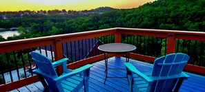 A deck with two chairs and a table, overlooking a forested area and a body of water.