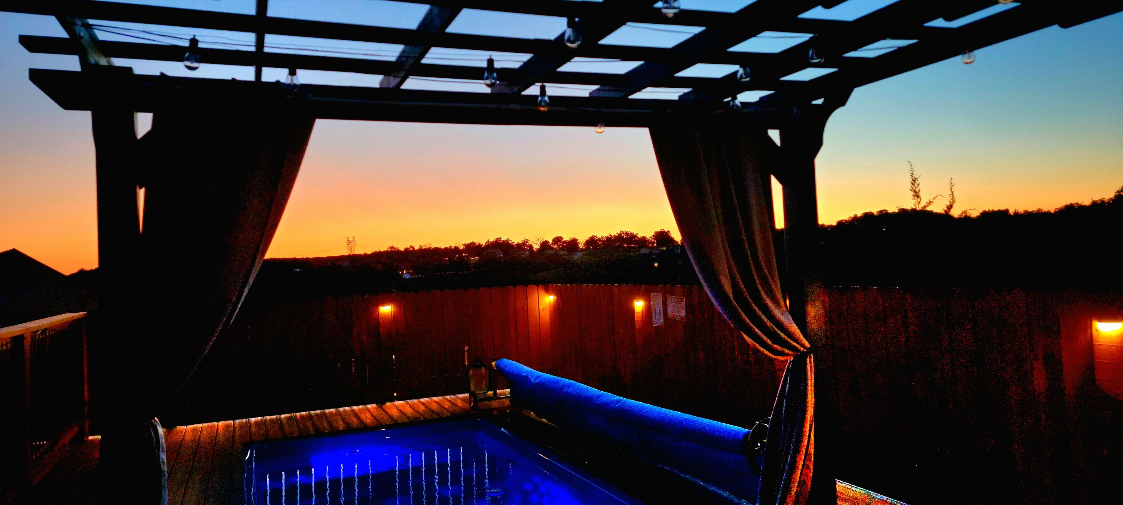 Un espace piscine offrant une vue sur le coucher de soleil, une pergola et une clôture en bois.