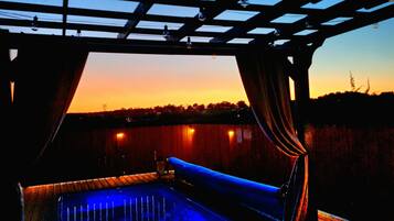 Un espace piscine offrant une vue sur le coucher de soleil, une pergola et une clôture en bois.