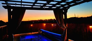 Een zwembad met uitzicht op de ondergaande zon, een pergola en een houten omheining.
