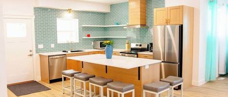 Een moderne keuken met een centraal eiland, barkrukken, roestvrijstalen apparatuur en een blauwgroene achterwand.