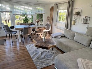 A modern living room with a wooden coffee table, grey sofa, and dining area with chairs and a table.