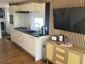 A modern kitchen with white cabinets, a black countertop, and a wooden cabinet with a TV above it.