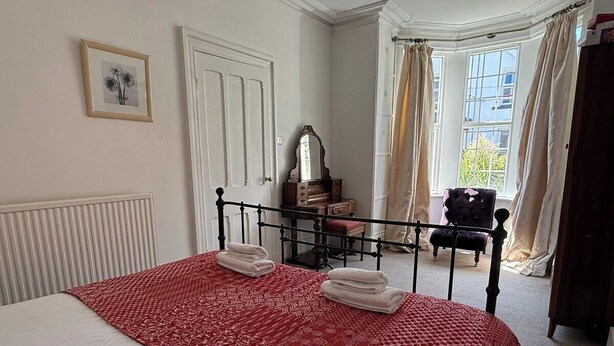Un dormitorio con cama, cómoda, espejo y ventana con cortinas.
