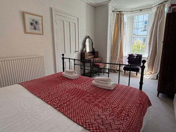 A bedroom with a bed, a dresser, a mirror, and a window with curtains.