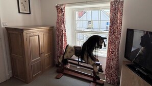 Una habitación con un caballito de madera, televisión y una ventana con cortinas.