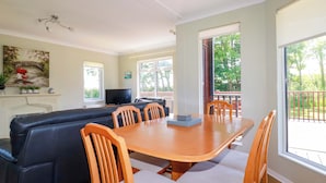 A dining area with a wooden table and chairs, a black sofa, and a television. - Lodge 9- Lamorna (Padstow)