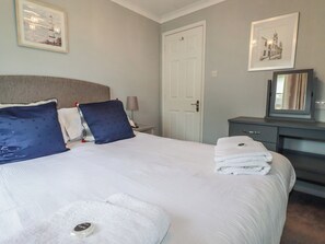 A neatly made bed with pillows, a bedside lamp, and a stack of towels.
