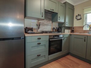 A kitchen with a stainless steel refrigerator, a stove, and a microwave. There are cabinets with handles and a window above the sink. - Lodge 9 - Lamorna (Padstow)