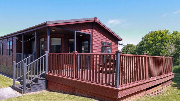 A red wooden cabin with a porch and stairs leading to a deck. - Lodge 9 - Lamorna (Padstow)