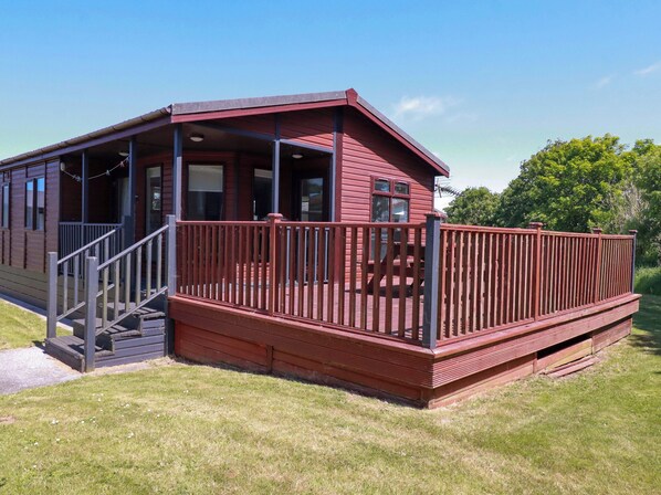 A red wooden cabin with a porch and stairs leading to a deck.