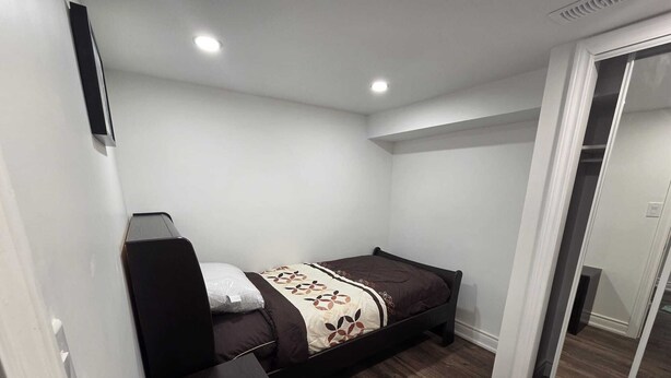 A small, neatly arranged bedroom with a bed, a desk, and a sliding door leading to another room. - Luxury 2-bed Suite (Mississauga)