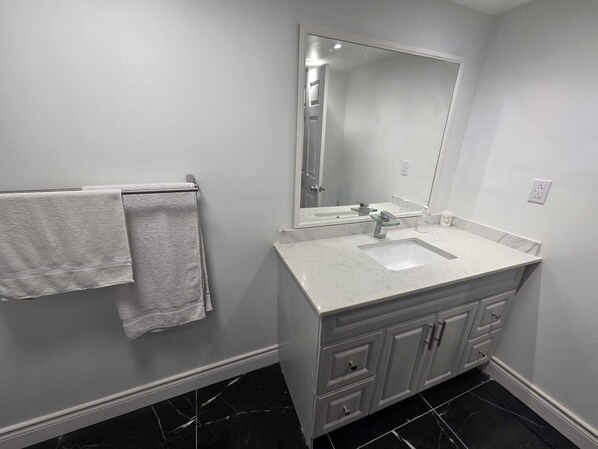 A bathroom with a white sink, a large mirror, and a towel rack with two towels. - Luxury 2-bed Suite (Mississauga)