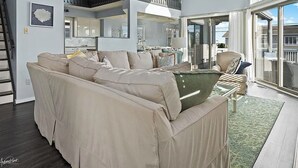 A spacious living area with a large beige sectional sofa, a dining table, and a staircase leading to an upper level. - Large 6 bedroom,7.5 bath house in Avalon, NJ-POOL  & Ocean Views- 3rd from beach (Avalon)