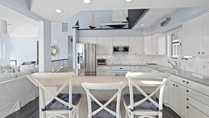 A modern kitchen with white cabinetry, a central island, and a dining area with white chairs. - Large 6 bedroom,7.5 bath house in Avalon, NJ-POOL  & Ocean Views- 3rd from beach (Avalon)