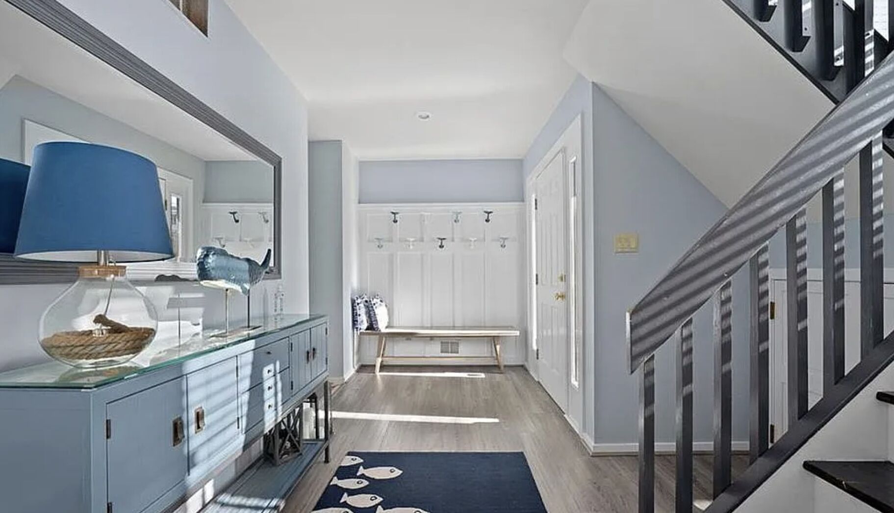 A modern hallway with a glass cabinet, a blue lamp, a fish bowl, and a staircase.