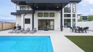 Ein modernes, zweistöckiges Haus mit Swimmingpool, Sitzgelegenheiten im Freien und einem gepflegten Rasen.