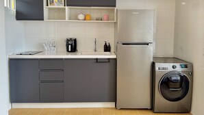 A modern kitchen with grey cabinets, a stainless steel refrigerator, a built-in washing machine, and a small shelf with decorative items.