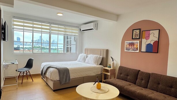 A modern hotel room with a bed, a sofa, a small table, and a desk.