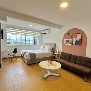 A modern hotel room with a bed, a sofa, a small table, and a desk.