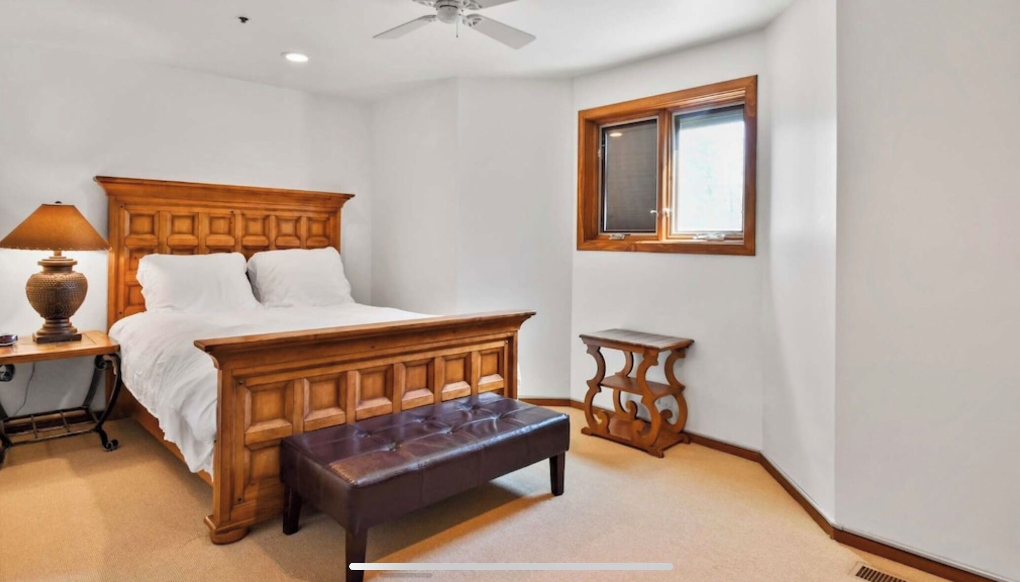 Une chambre à coucher avec un lit en bois, une table de chevet avec une lampe, un banc et une fenêtre.