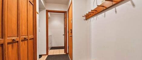 A hallway with wooden doors, a small table, and a shelf with hooks.