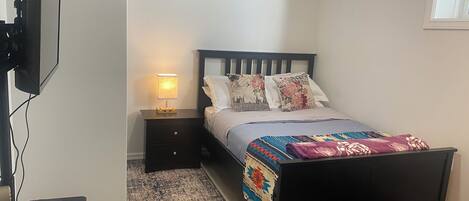 Un dormitorio con cama, mesita de noche, televisor y una alfombra.