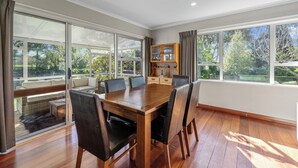A dining area with a wooden table and chairs, large windows, and a view of greenery outside.