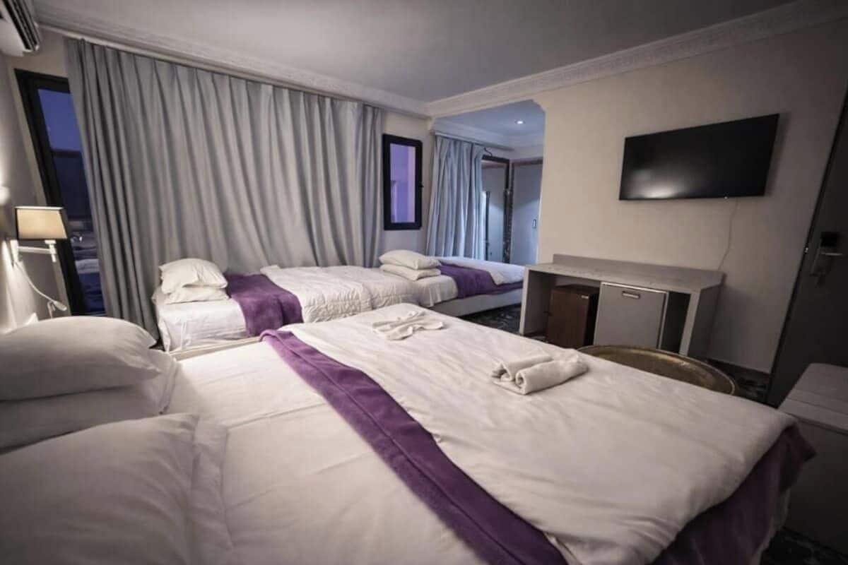 Habitación de hotel con dos camas, televisión, escritorio y ventana con cortinas.