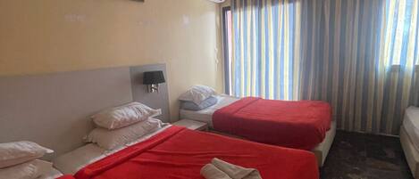 A hotel room with two beds, a nightstand, an air conditioning unit, and a window with striped curtains.
