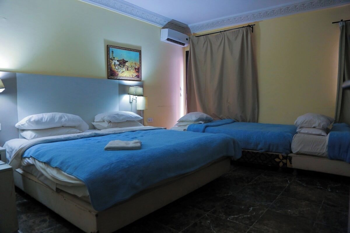 Une chambre d’hôtel avec deux lits, un tableau au mur, un appareil de climatisation et un rideau.