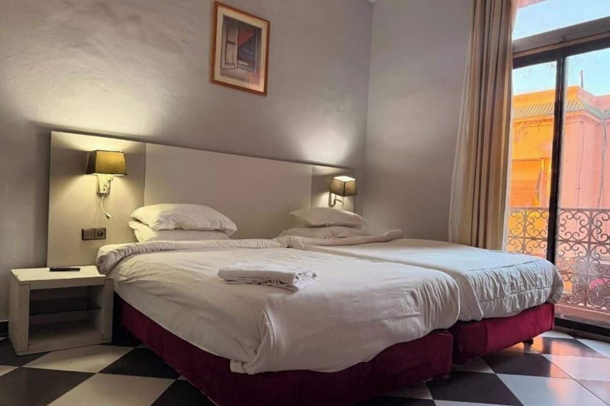 Habitación de hotel con una cama grande, dos lámparas de noche, una mesita de noche y vistas a un edificio a través de una ventana.