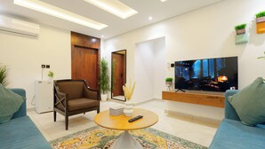 A modern living room with a sofa, a coffee table, a TV, and a small refrigerator. - Lavida luxe Apartments  (Riyadh)