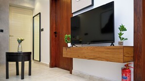 A modern living room with a flat-screen TV mounted on a wooden wall, a small table with a vase, and a fire extinguisher on the floor. - Lavida luxe Apartments  (Riyadh)