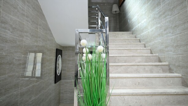 A modern staircase with a metal railing, a wall-mounted clock, and a planter with green plants and white spherical decorations. - Lavida luxe Apartments  (Riyadh)
