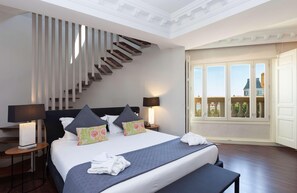 A hotel room with a large bed, a staircase, two bedside lamps, a nightstand, and a view of a building through a window. - Sardinero Madrid (Madrid)