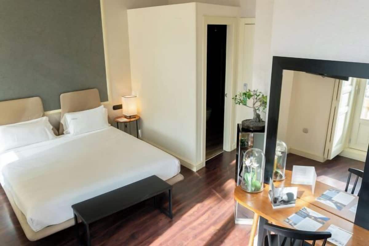 Une chambre d’hôtel avec un lit, une table de chevet, une lampe et un bureau avec des papiers.