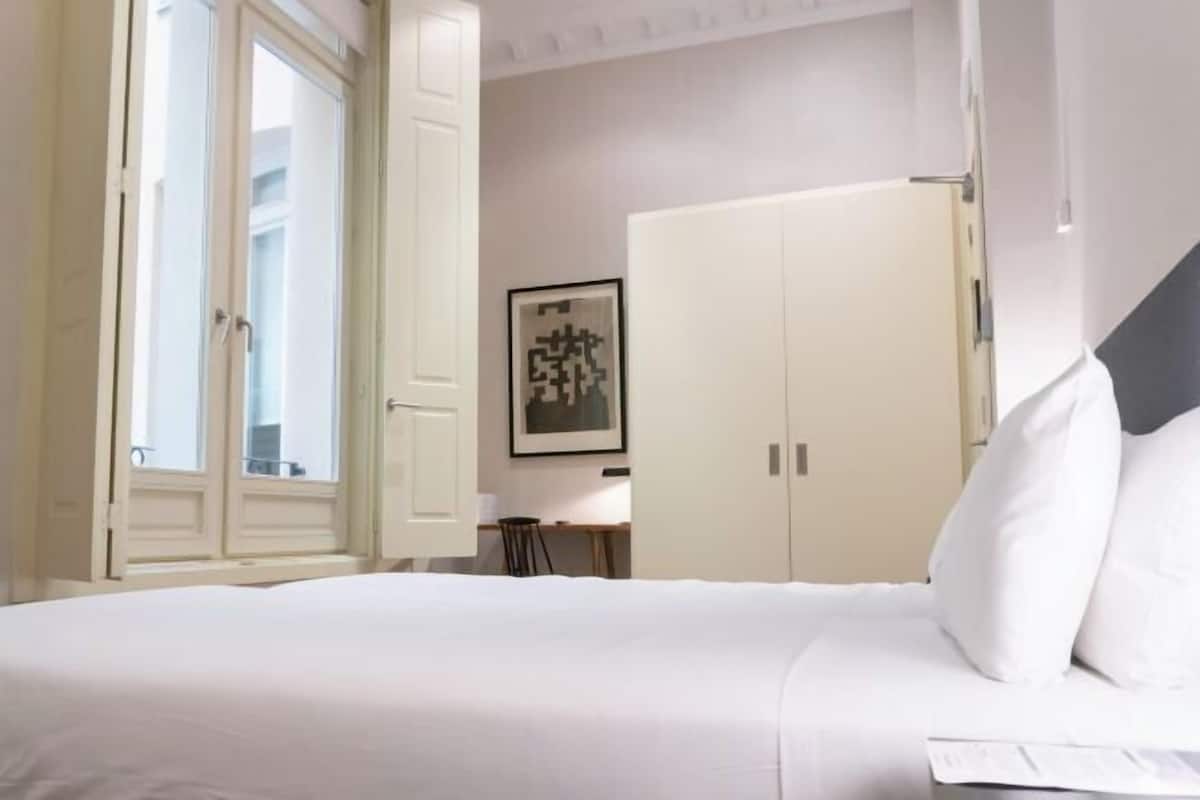 Une chambre d’hôtel avec un lit, un bureau, une chaise, une armoire et une fenêtre.